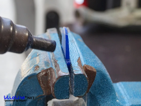 Una barbette in plastica blu da saldare al rivestimento in plastica della protezione dello zoccolo è fissata in una morsa e viene riscaldata con una pistola ad aria calda dotata di ugello riduttore.