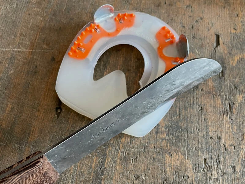 Detailaufnahme der Klinge der Double S Hauklinge Kukri. Auf dem Bild sieht man dass mit der Klinge der Kunststoffmantel eines Verbundhufeisens für Pferde angepasst werden soll. Das Hufeisen liegt auf einer Werkbank.