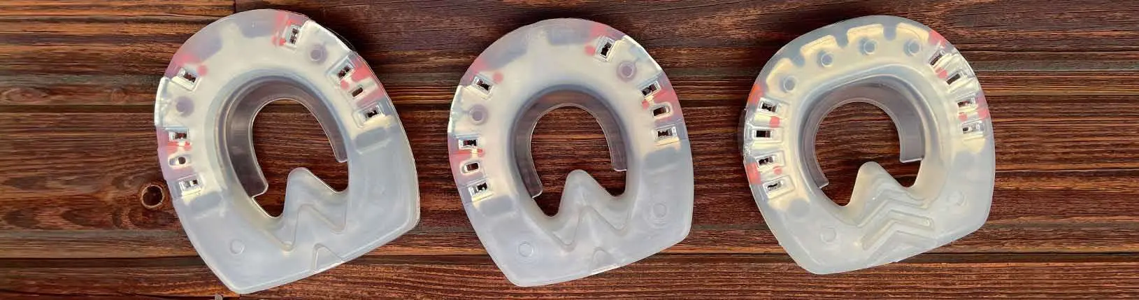 Drei verschiedene Formen eines Kunststoffbeschlags mit Metallkern und Seitenkappen – rund, oval und STS-Form – liegen auf einem Holzbalken.