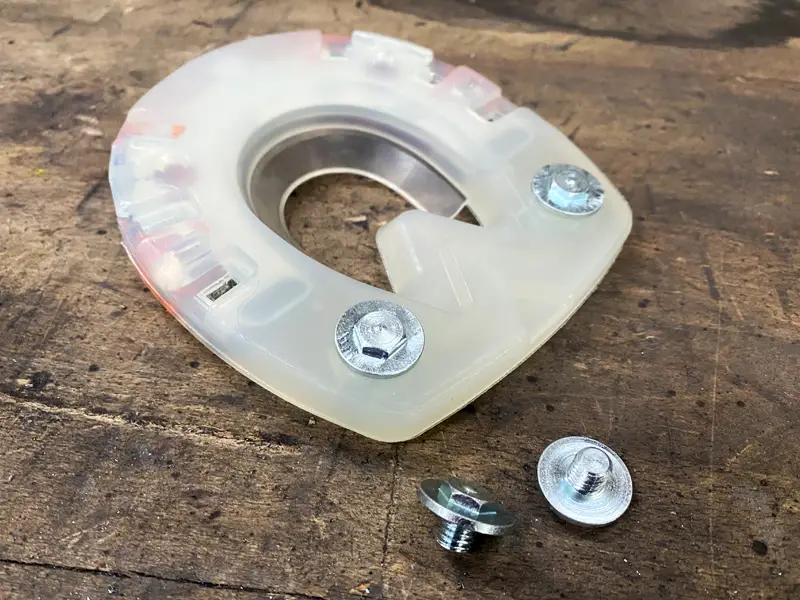 Un ferro composito con due ramponi avvitati con collarino per una protezione antiscivolo aggiuntiva è posizionato su un banco da lavoro accanto ad altri due ramponi a vite.