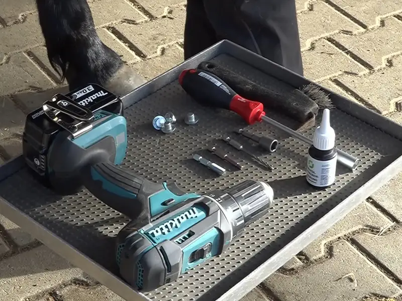 Su un piccolo banco da lavoro si trovano un avvitatore Makita, un fissavite Reidl, ramponi per cavalli e diversi inserti per il montaggio dei ramponi.