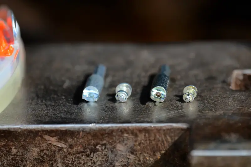 Gleitschutz für Hufeisen mit Kunststoffmantel: Spikes mit Adapter für Plastikbeschläge liegen auf einem Amboss.