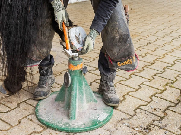 Maniscalco applica un ferro in plastica con anima in metallo sullo zoccolo di un cavallo. Lo zoccolo poggia sull'appoggio posteriore di un Hoofjack® verde.