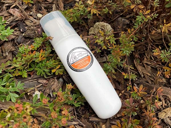 Un flacon pinceau de Hoofsmooth est posé sur un sol couvert de branches.