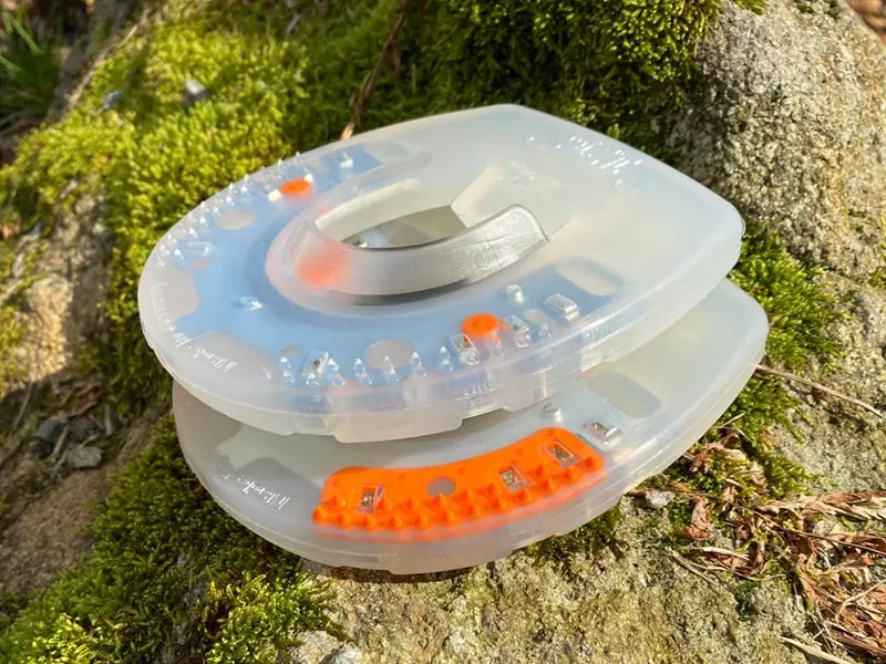 Deux fers avec enveloppe en plastique sans pinçons latéraux reposent sur une pierre recouverte de mousse. Le fer supérieur est le Duplo Nailless sans insert à nodules rigide, en dessous se trouve un Duplo Standard avec insert à nodules orange.