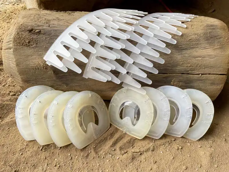 Huit fers factices sont posés dans le sable devant une bûche sur laquelle reposent huit colliers adhésifs.
