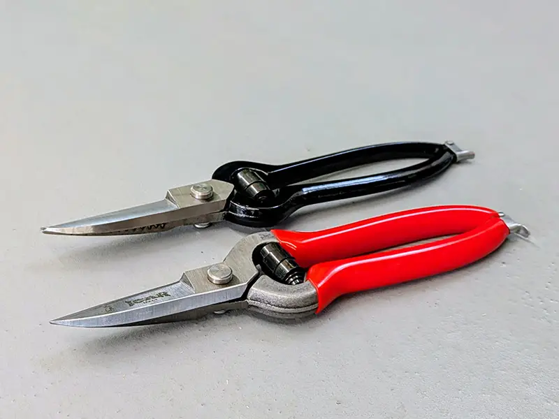Immagine della cesoia nera Blacksmith e della cesoia rossa ICAR, affiancate su un pavimento in cemento.
