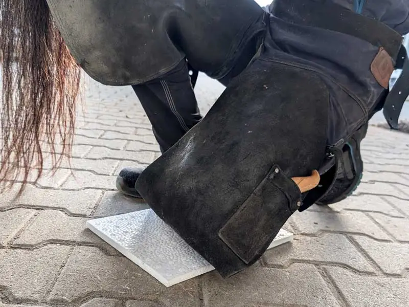 Durante il lavoro sullo zoccolo del cavallo, il maniscalco è inginocchiato su una piastra ammortizzante rettangolare, per evitare che il ginocchio poggi direttamente sul pavimento duro.