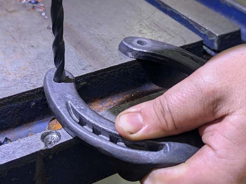 Un trou est percé dans un fer à cheval à l'aide d'un foret en acier afin d'insérer ensuite les crampons à enfoncer.