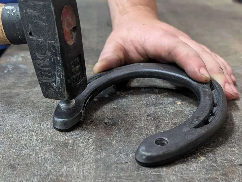 Le maréchal-ferrant frappe un crampon à enfoncer avec un marteau pour le fixer dans le fer à cheval.