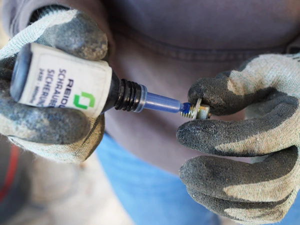 Detailaufnahme beim Auftragen von einem Tropfen EURO-LOCK Schraubensicherung auf einen Gleitschutz-Stollen für Verbund-Hufeisen.