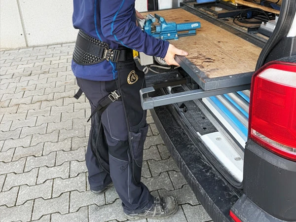 Ein Hufschmied trägt die Hufschmiedeschürze Original Pro von Silverback. Er steht am Beschlagswagen.