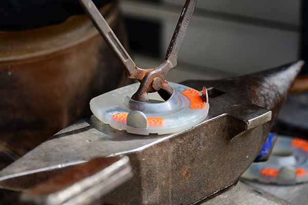 Der Hufschmied weitet ein alternatives Hufeisen mit einer Feuerzange, um es an die Hufform des Pferdes anzupassen; das Hufeisen liegt auf dem Amboss.