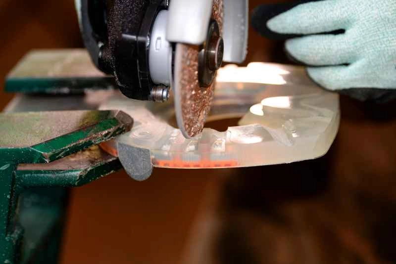 Der Hufschmied trägt Schnittschutzhandschuhe und schleift mit einem Winkelschleifer ein verstärktes Profil in den Kunststoffmantel des alternativen Hufeisens. Das Hufeisen ist in einem Schraubstock fixiert.