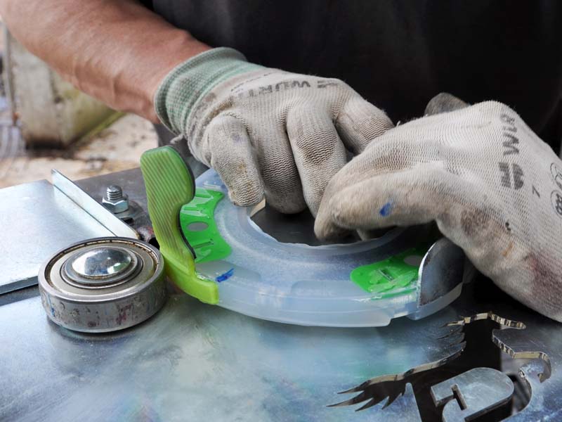 Des mains portant des gants de travail enroulent une ferrure avec des pinçons latéraux autour du roulement à billes d'un dispositif spécial pour souder la patte de collage.