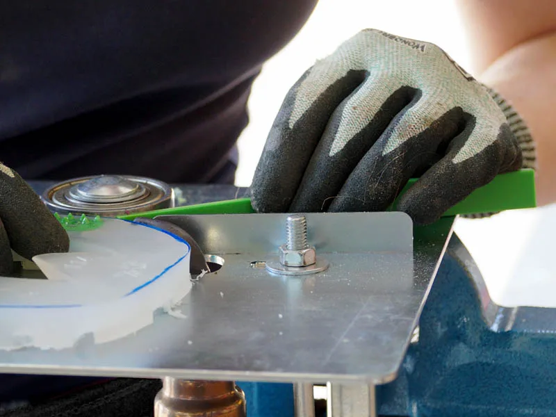 Hände mit Schnittschutzhandschuhen halten einen Kunststoffbeschlag und einen grünen Farbstreifen beim Verschweissen mithilfe einer besonderen Vorrichtung